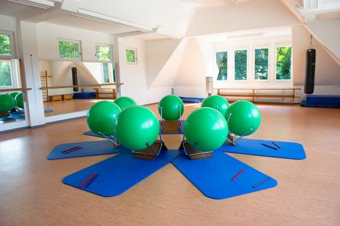Fitnessraum mit grünen Gymnastikbällen auf blauen Matten, umgeben von Spiegeln und Fenstern.