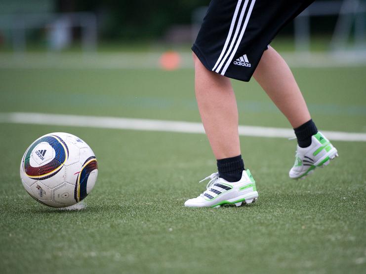 Ein Fuß mit Fußballschuhen tritt auf einen Fußball auf einem Kunstrasenfeld.