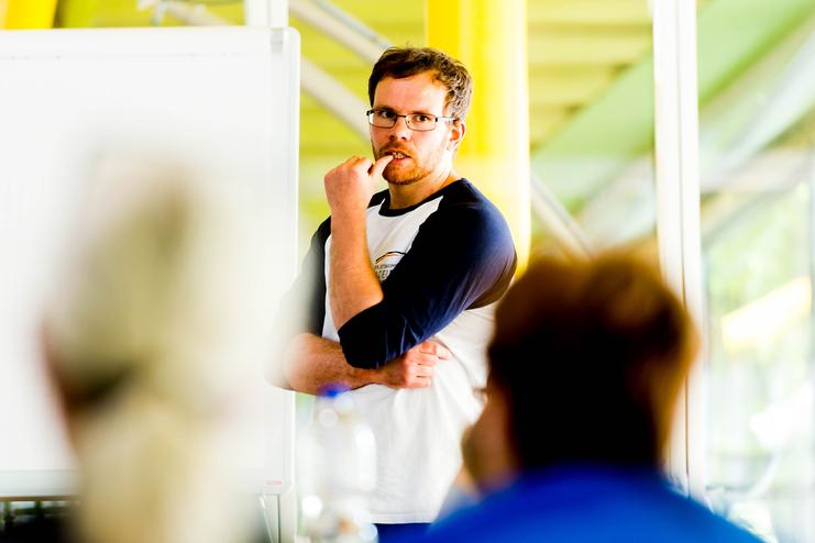 Mann mit Brille spricht vor einer Gruppe, ein Flipchart ist im Hintergrund sichtbar.